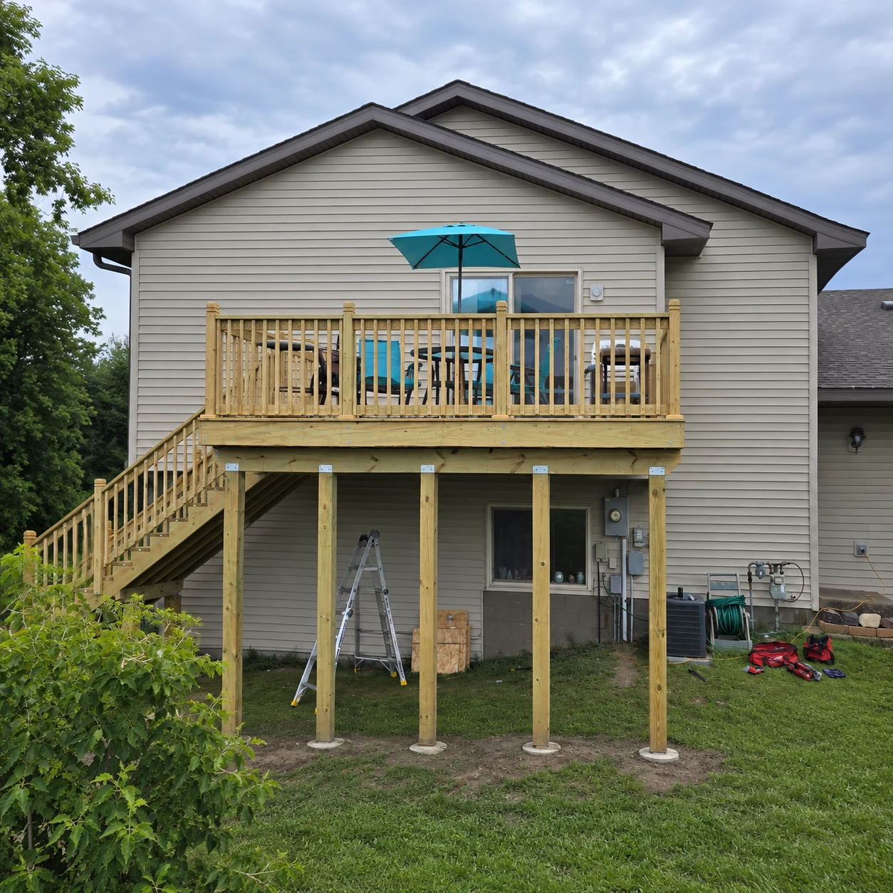 Raised wood deck with vertical railings and a staircase beside a home